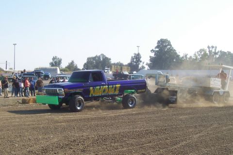 1994 Ford F-150 - A modified pickup truck, likely from the late 1970s, competes in a pulling event, kicking up dust.