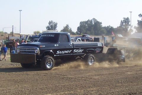 1994 Ford F-150 - A modified Ford pickup truck competes in a sled-pulling event, kicking up dust as it moves forward.