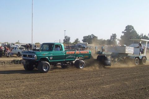 1994 Ford F-150 - A modified green pickup truck, identified by its body style as likely from the early 1970s, competes in a pulling event, dragging a weighte…