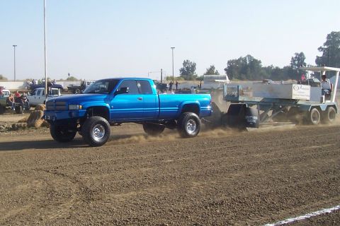 1994 Ford F-150 - Blue Dodge Ram pickup truck competes in a pull event, dragging a sled across a dirt track.