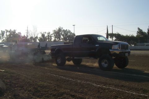 1994 Ford F-150 - A lifted black pickup truck tows a trailer across a dirt track under a bright sky.