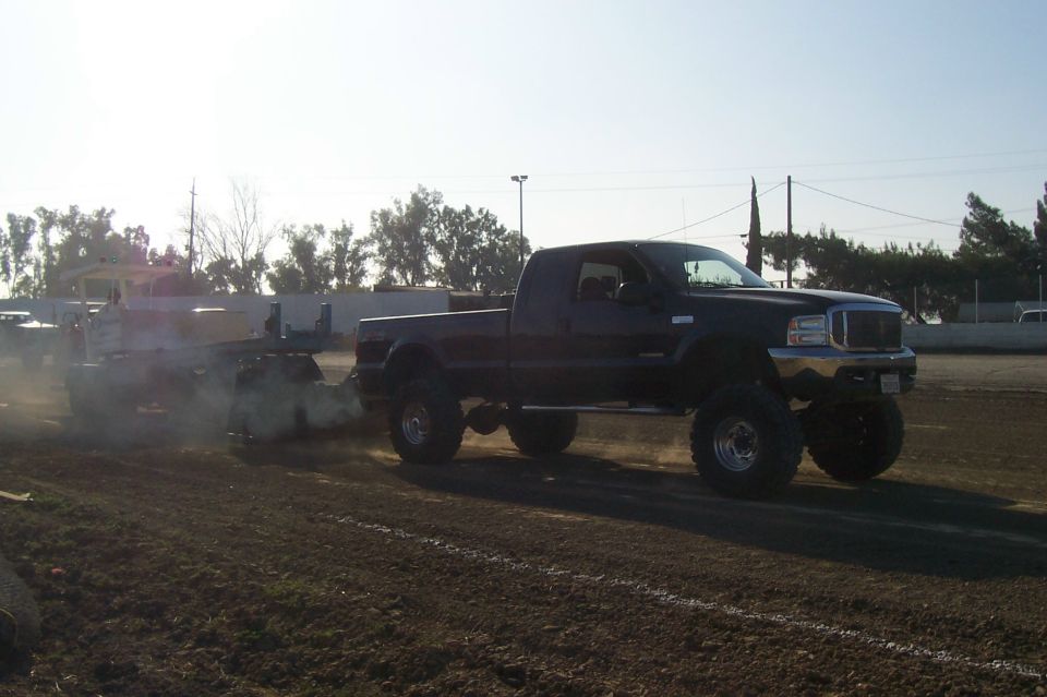 Black lifted pickup truck towing a trailer on a dirt track, front grille visible