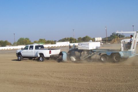 1994 Ford F-150 - A white dually pickup truck pulls a sled in a dirt arena, kicking up dust.