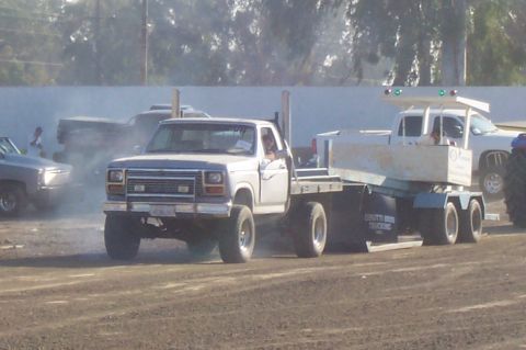 1994 Ford F-150 - Ford F-Series truck from the 1980s towing a trailer, with other vehicles and smoke in the background.