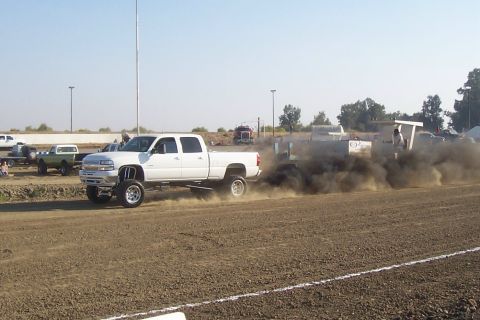 1994 Ford F-150 - A white pickup truck competes in a pull event, generating significant exhaust smoke as it drags a sled across the dirt track.