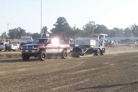 1994 Ford F-150 - A red pickup truck tows a sled during a competition in a dirt arena.