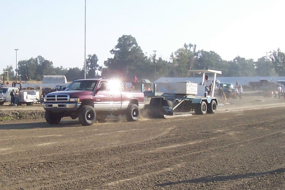 Red pickup truck towing a sled in a dirt arena. Year is 1994