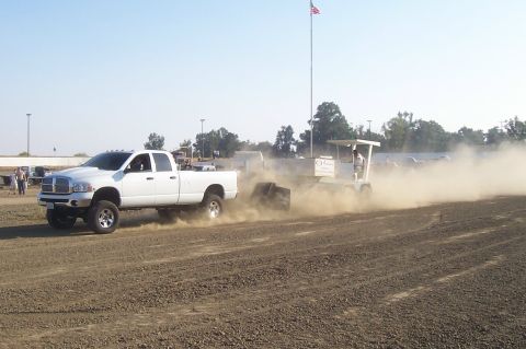 1994 Ford F-150 - White Dodge Ram pickup truck competes in a sled pull event, kicking up dust.