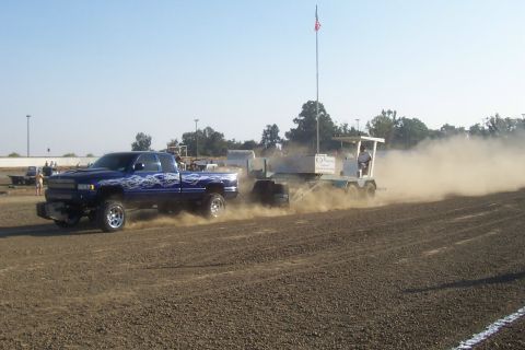 1994 Ford F-150 - A blue Dodge Ram truck is seen pulling a sled in a dirt arena, creating a large dust cloud.