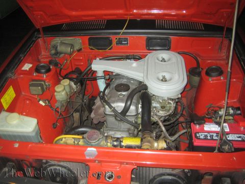 1968 Ford Mustang - The engine bay of a red car shows a carburetor, air filter, and battery.