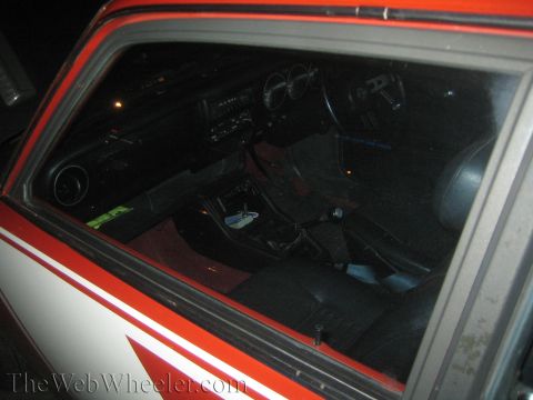 1968 Ford Mustang - The interior of a red and white vehicle is visible through the window, revealing the dashboard and seating areas of the cabin.