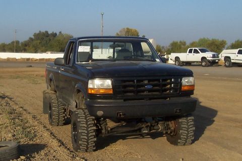 1994 Ford F-150 - Lifted 1994 Ford F-150 pickup truck in a dirt lot with other vehicles present.