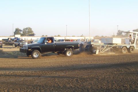 1994 Ford F-150 - A lifted black pickup truck is seen from the side, pulling a trailer across a dirt track, kicking up dust.