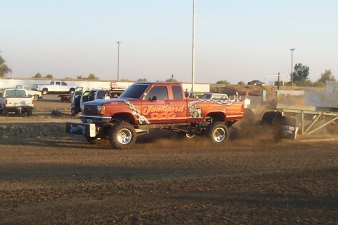 1994 Ford F-150 - A lifted pickup truck with custom graphics competes in a pull event, kicking up a cloud of dirt.