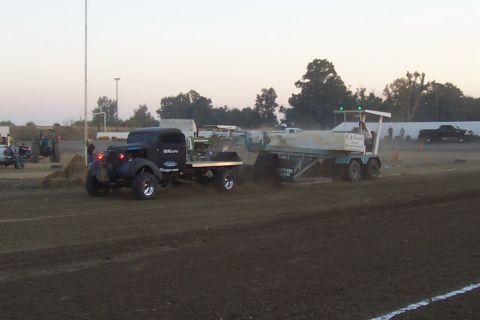 1994 Ford F-150 - A black pickup truck, possibly a modified classic, tows a trailer across a dirt track during an event.