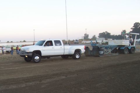 1994 Ford F-150 - White dually pickup truck tows a sled on a dirt track, with other vehicles and people in the background.