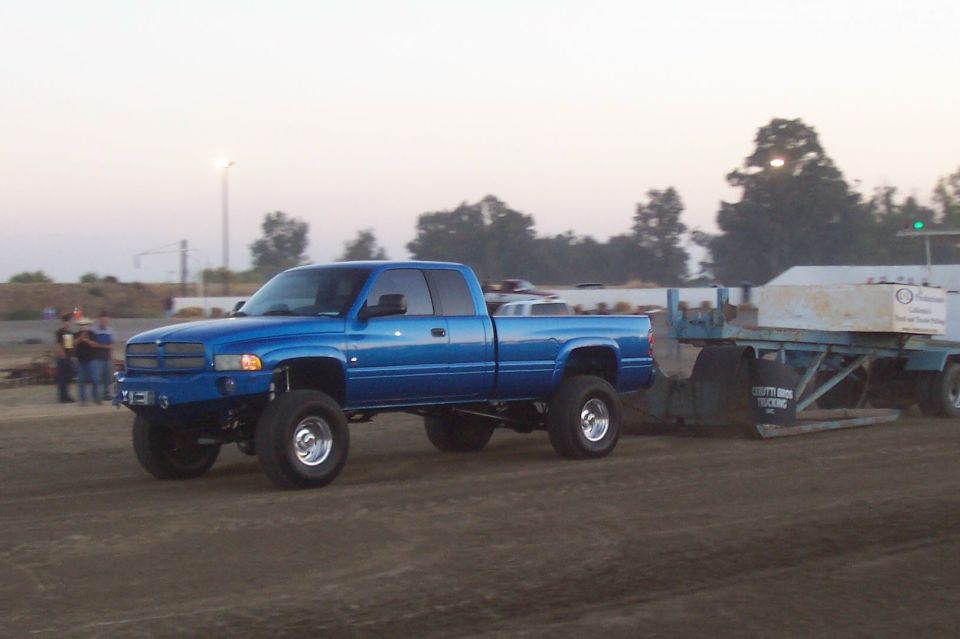 Blue Dodge Ram pickup truck with lifted suspension, towing a trailer with concrete blocks