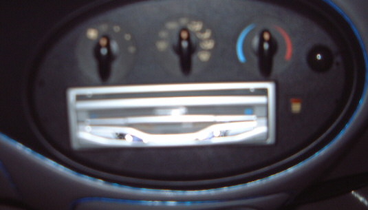 Blurry dashboard climate control panel with three rotary knobs over a vent