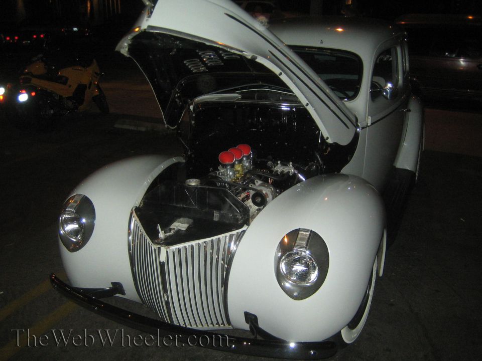 White 1939 Ford sedan, front view, hood open revealing engine. Chrome grille and headlights