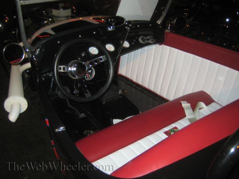 1968 Ford Mustang - The interior of a custom hot rod features a black dashboard, red and white seats, and a large exhaust pipe.