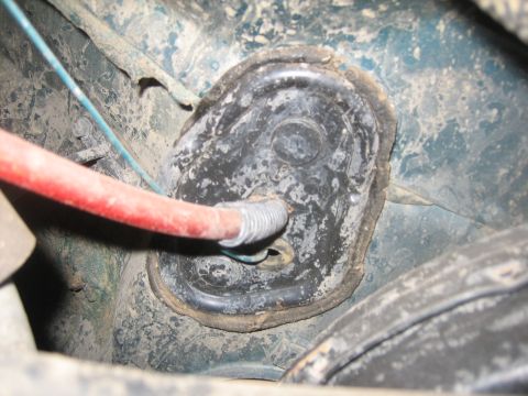 1995 Ford Bronco - A close-up view of a vehicle's undercarriage component, showing a red hose and wiring harness attached to a rubber mount.