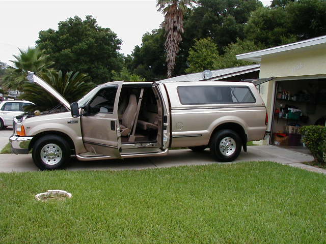 Tan Ford Super Duty extended cab pickup with doors open, hood up and matching camper shell