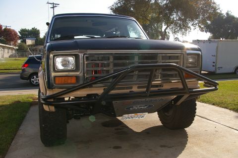 1986 Ford Bronco - A dark blue Ford Bronco with a tan lower body and a custom black bumper is parked on a driveway.