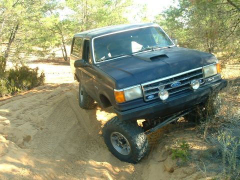 1995 Ford Bronco - Blue Ford Bronco navigating a sandy trail with its front wheels elevated.