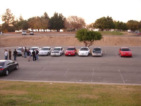 1993 Ford Taurus - Several cars are parked in an outdoor lot with trees and a grassy hill in the background.