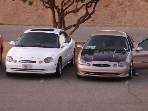 1993 Ford Taurus - Two Ford Taurus sedans are parked in a lot, one white and the other tan with a contrasting black hood.