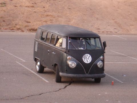 1993 Ford Taurus - A black Volkswagen Type 2 Bus is parked in a cracked asphalt lot with a dry, brown hillside in the background.