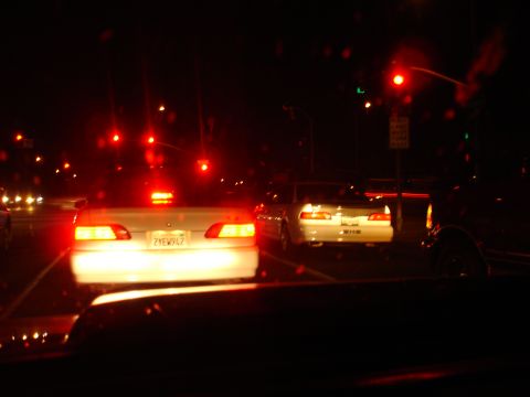 1993 Ford Taurus - A white sedan is seen from behind at night, with its brake lights illuminated. Another vehicle is ahead in traffic.