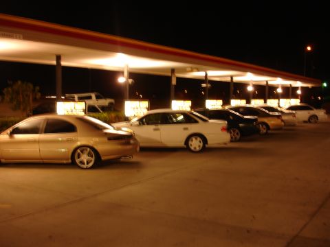 1993 Ford Taurus - Several sedans are parked in a row under a covered structure at night.