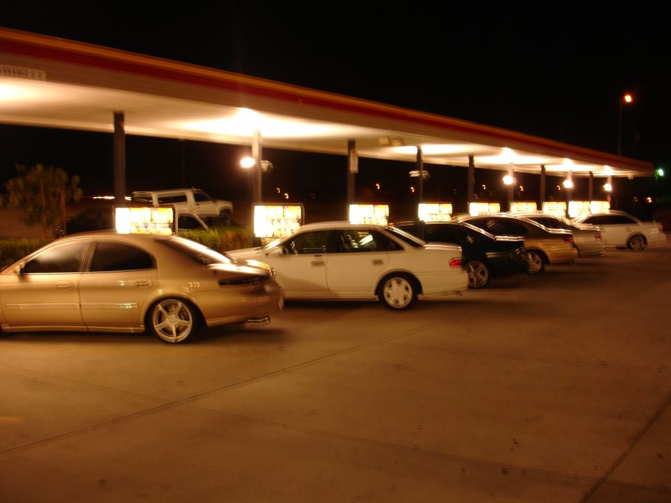 Gold sedan parked at night, side view. Other cars are visible behind it