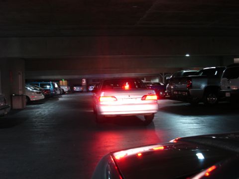 1993 Ford Taurus - A silver sedan's brake lights illuminate the concrete floor of a parking garage, with other vehicles visible.