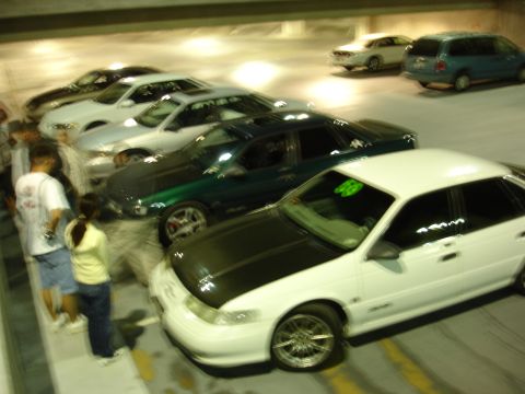 1993 Ford Taurus - A white 1993 Ford Taurus with a black hood is parked in a lot alongside other vehicles.