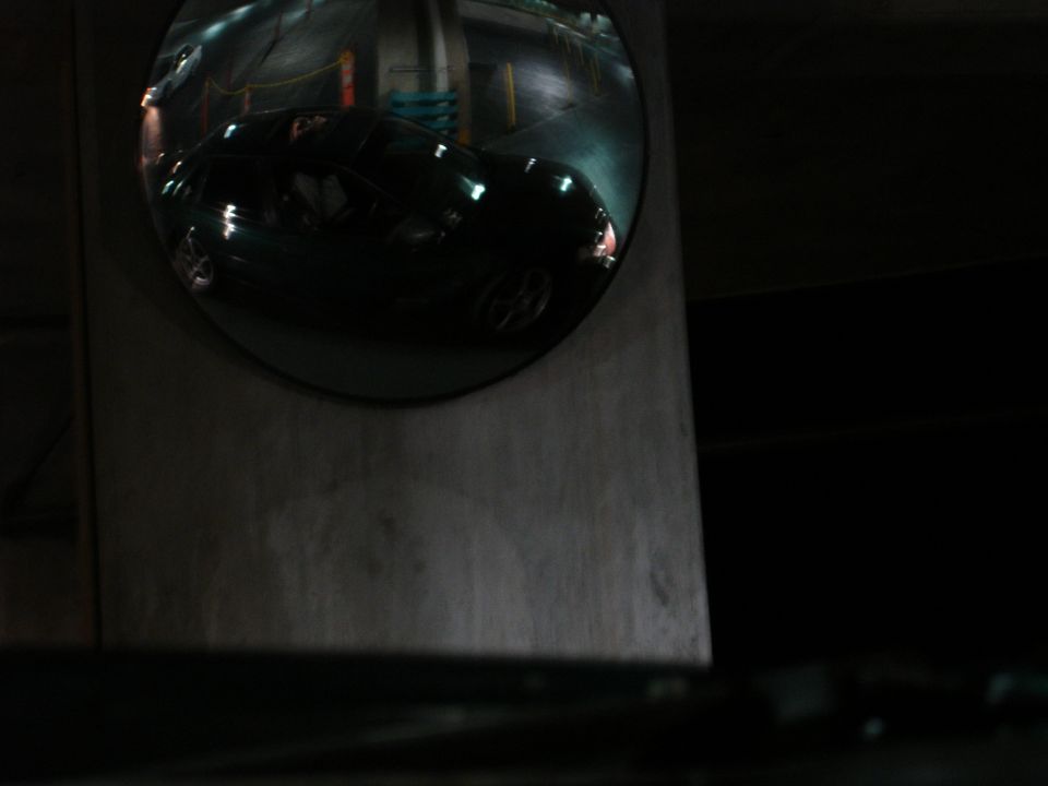 Dark sedan reflected in a convex mirror in a parking garage