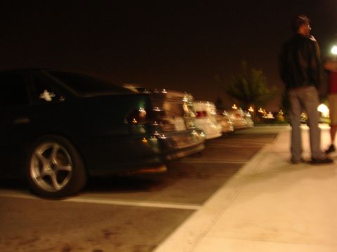1993 Ford Taurus - Several cars are parked in a lot at night, with a dark sedan in the foreground.