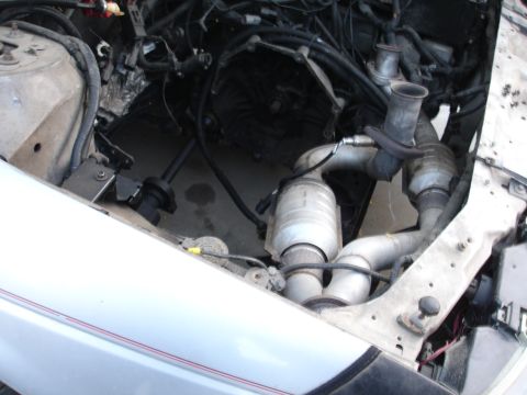 1993 Ford Taurus - The engine compartment of a car is shown, revealing the transmission and exhaust system with catalytic converters.