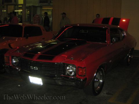1968 Ford Mustang - Red 1970 Chevrolet Chevelle SS with black racing stripes and hood scoop. Another vehicle is parked to the left.
