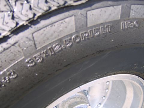 1989 Ford Bronco - Tight close-up of a wet tire sidewall showing the molded size marking 35X12.50R15LT with an aggressive lugged tread edge above and a polish…