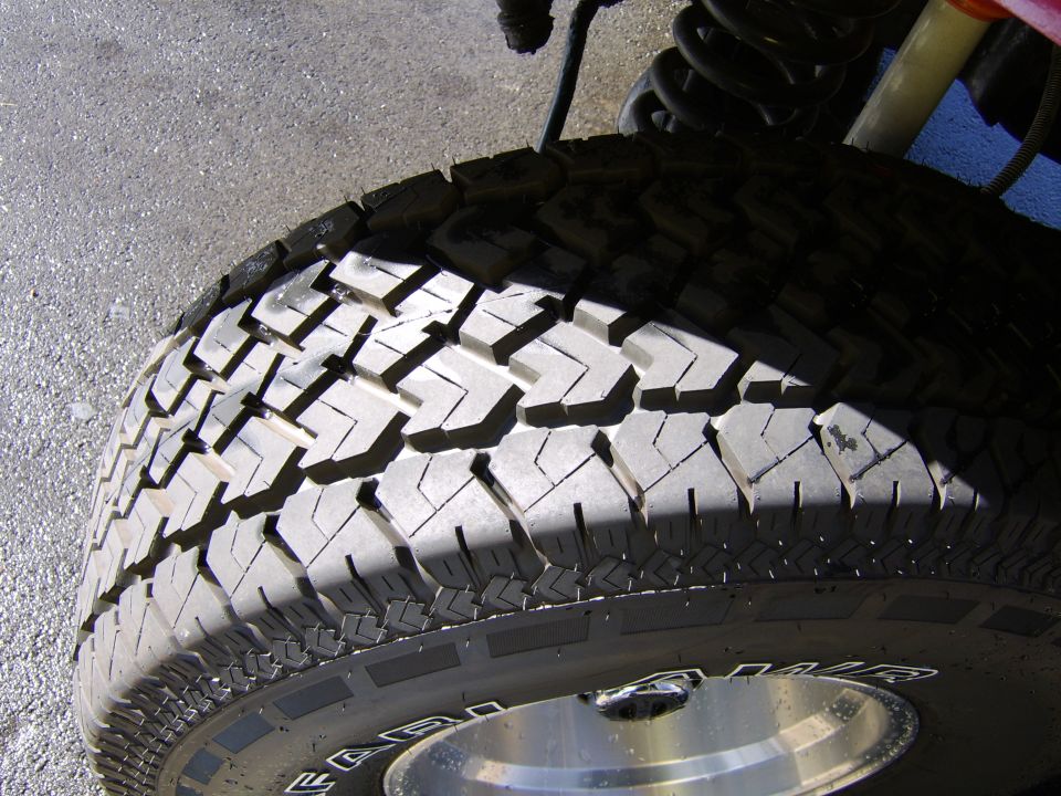Close-up of chevron-tread all-terrain tire on polished aluminum wheel with coil spring above