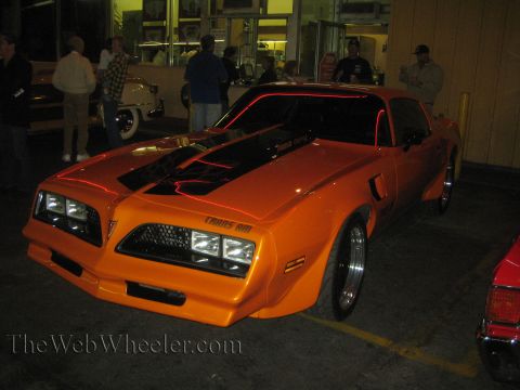 1968 Ford Mustang - This orange Pontiac Trans Am, likely a 1977 model, features black racing stripes and distinctive red accent lighting along its body.