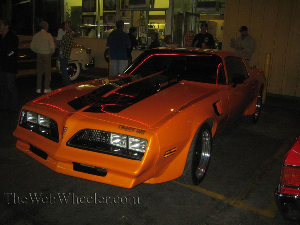 Orange 1977 Pontiac Trans Am with black racing stripes and red accent lighting