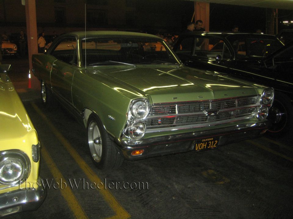 Green 1966 Ford Fairlane with a chrome grille and dual headlights, parked indoors