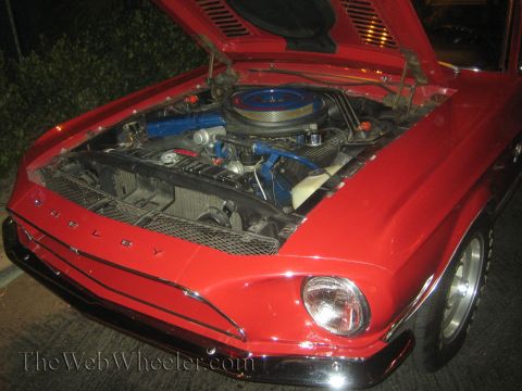 1968 Ford Mustang - The front of a red 1968 Ford Mustang Shelby is shown with its hood open, revealing the engine bay and prominent 'SHELBY' lettering.