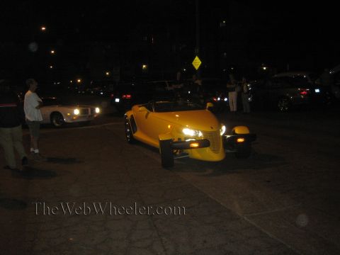1968 Ford Mustang - A yellow convertible is parked on a street at night, with other vehicles and people in the background.