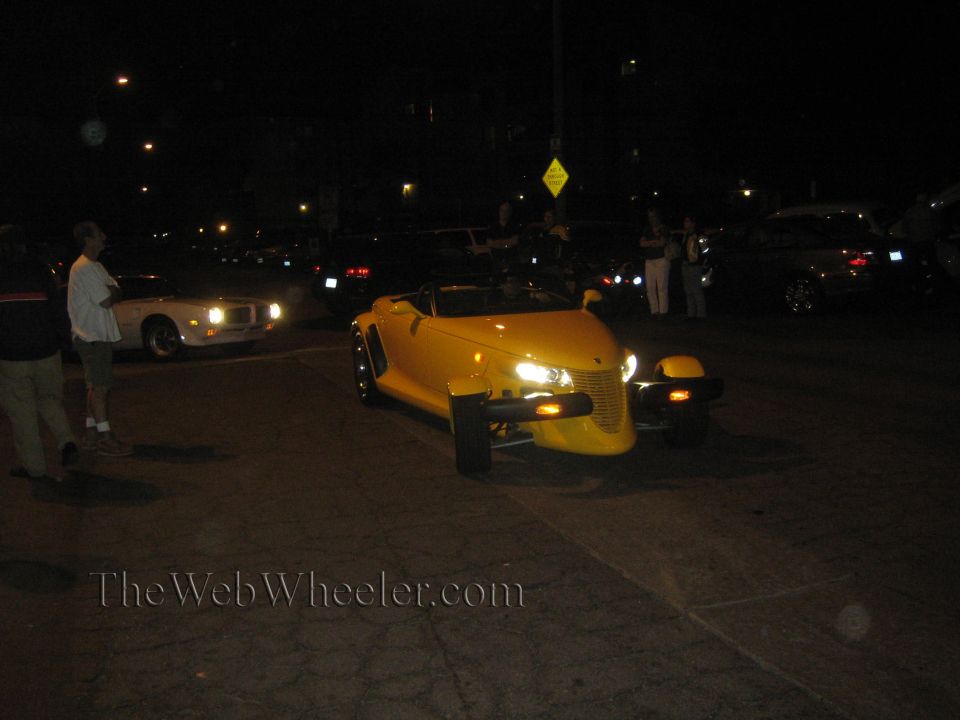 Yellow convertible with exposed wheels and a prominent grille, seen at night