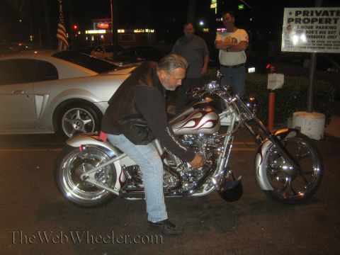 1968 Ford Mustang - A man inspects a custom chopper motorcycle, with a silver Ford Mustang visible in the background.
