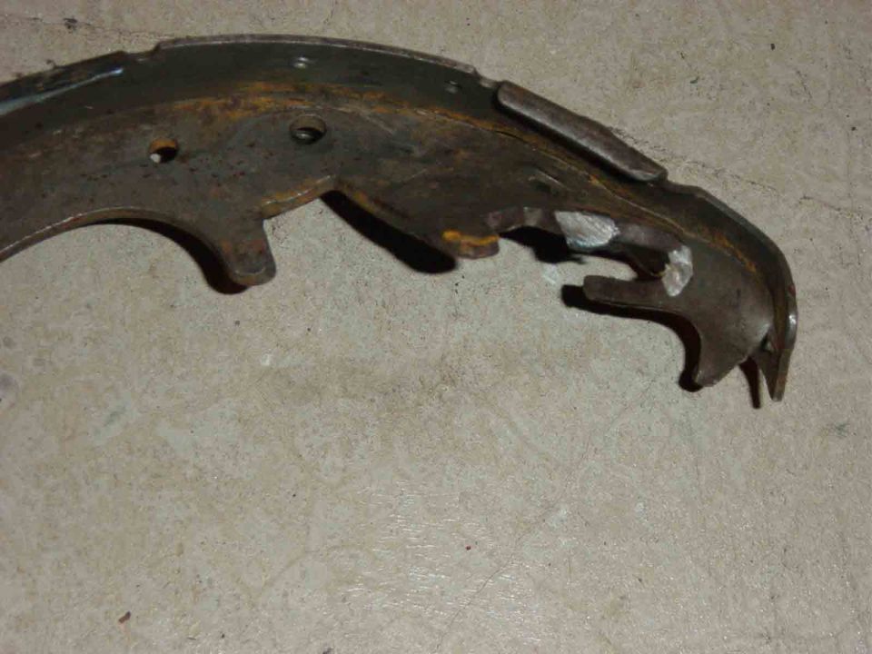 Rusty curved brake shoe with worn yellow paint lying on a concrete floor